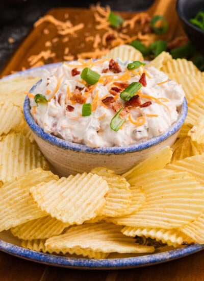 Close-up of loaded bacon cheddar dip with green onions and potato chips.