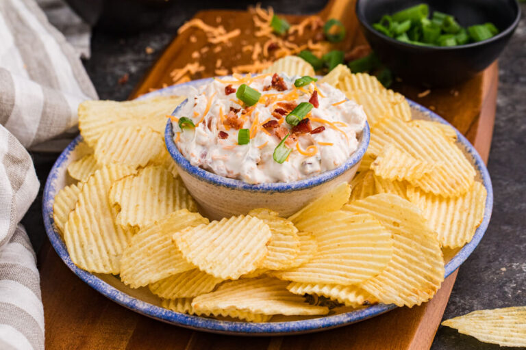 Close-up of loaded bacon cheddar dip with green onions and potato chips.