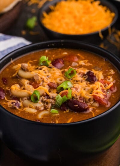 Hearty beef and bean macaroni soup in a black bowl, garnished with melted cheddar cheese and sliced green onions.