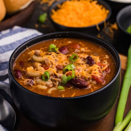 Hearty beef and bean macaroni soup in a black bowl, garnished with melted cheddar cheese and sliced green onions.
