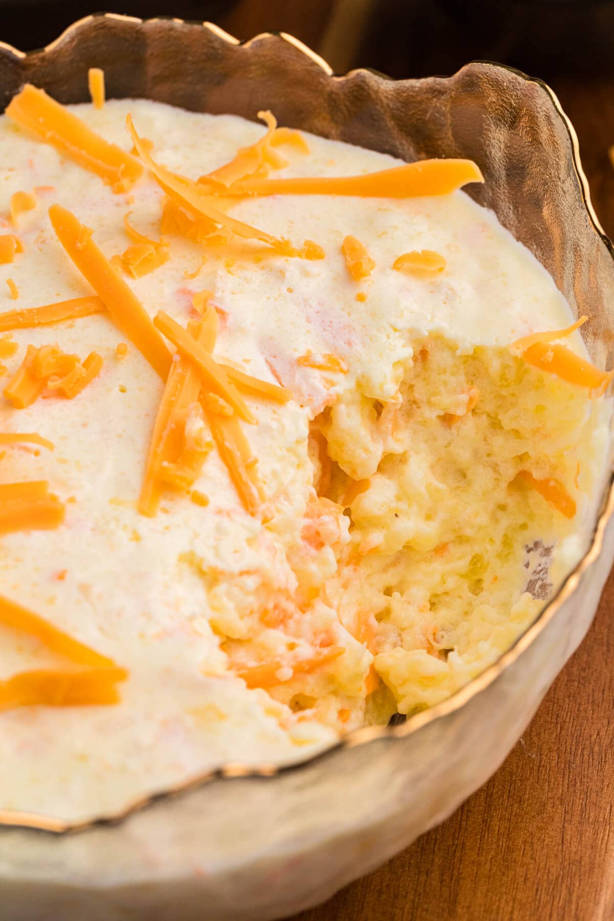 Partially scooped pineapple and cheese salad in a glass bowl, revealing the fluffy, creamy interior with carrot bits and cheddar cheese shreds.