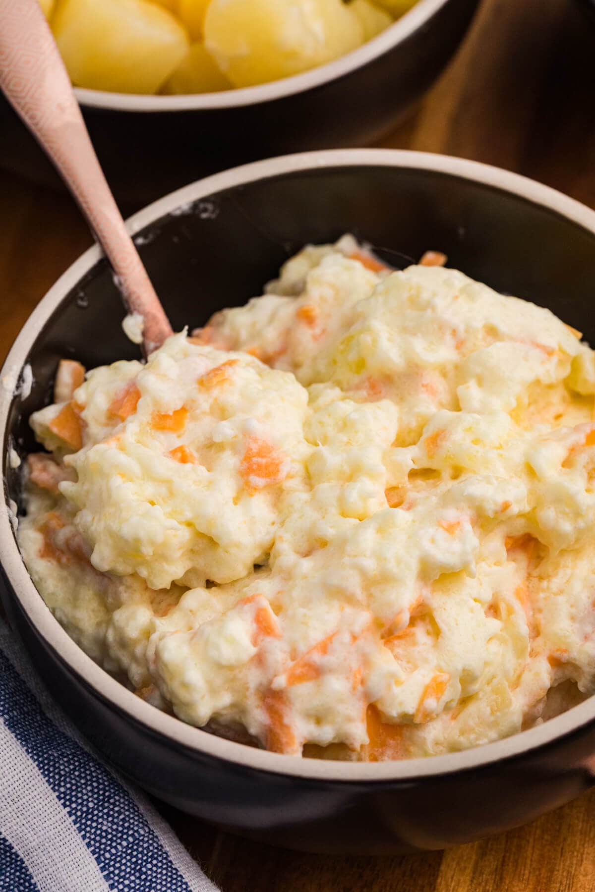 Creamy fruit and cheese salad served in a black bowl, showcasing a mix of pineapple, grated carrots, and a fluffy whipped texture, with a spoon inside.