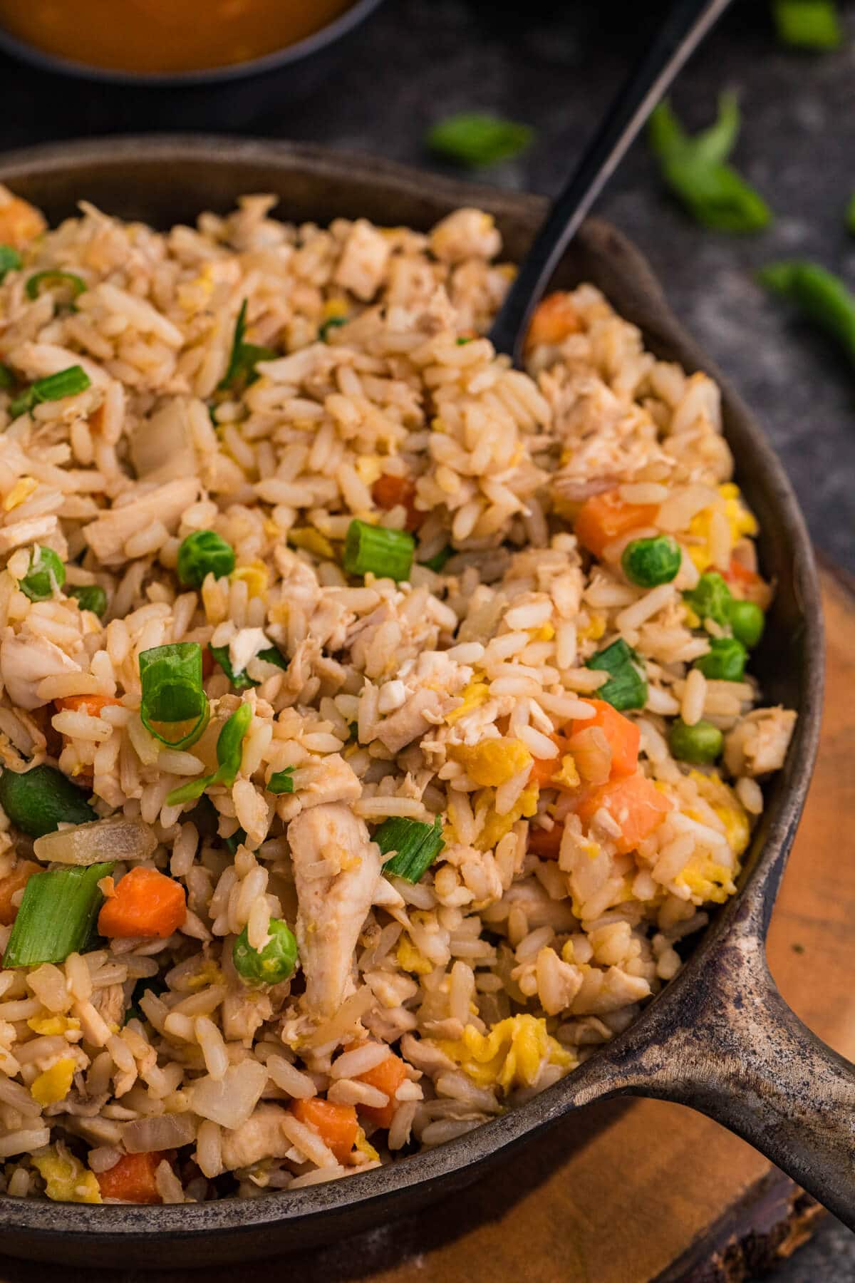 Close-up of chicken fried rice with diced vegetables, egg, and green onions in a rustic skillet.