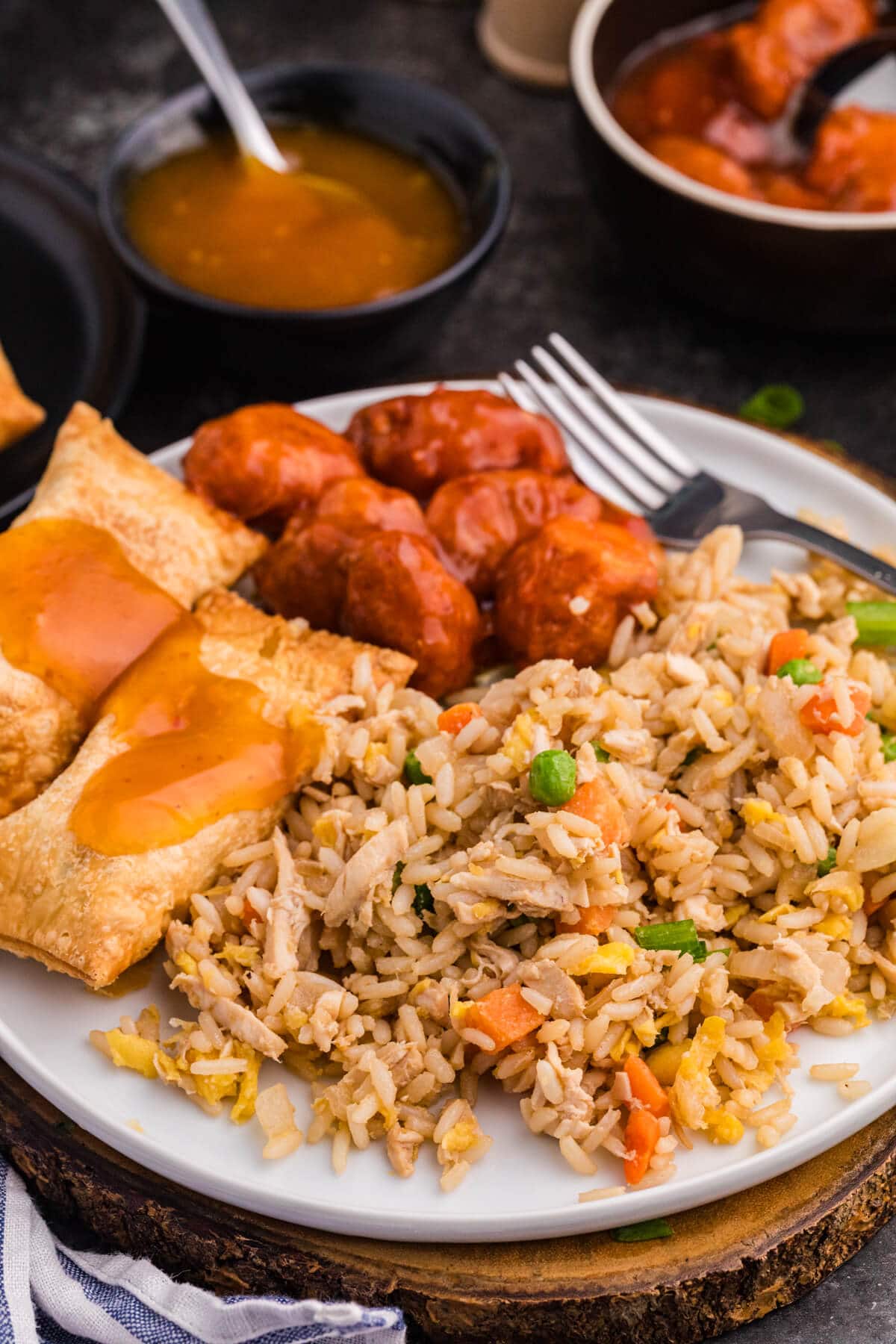 Plate of chicken fried rice with egg rolls topped in sauce and sweet-and-sour chicken bites.