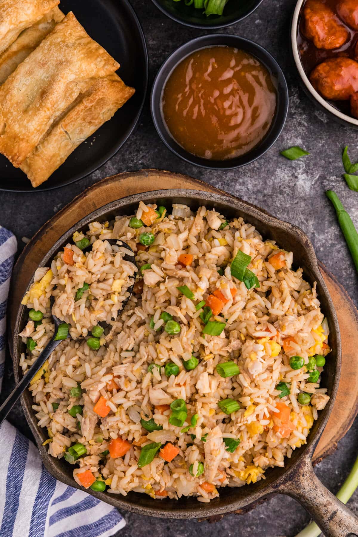 Rotisserie Chicken Fried Rice in a cast iron skillet with peas, carrots, egg, and green onions, served with egg rolls and dipping sauces.