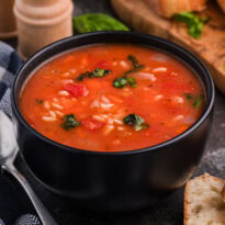 Bowl of vegetable rice soup with tomatoes and herbs, served with crusty bread.