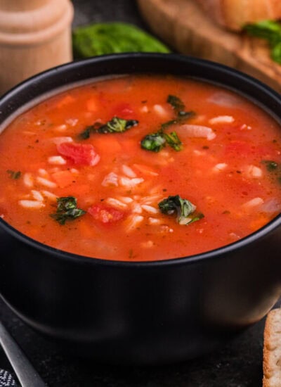 Bowl of vegetable rice soup with tomatoes and herbs, served with crusty bread.