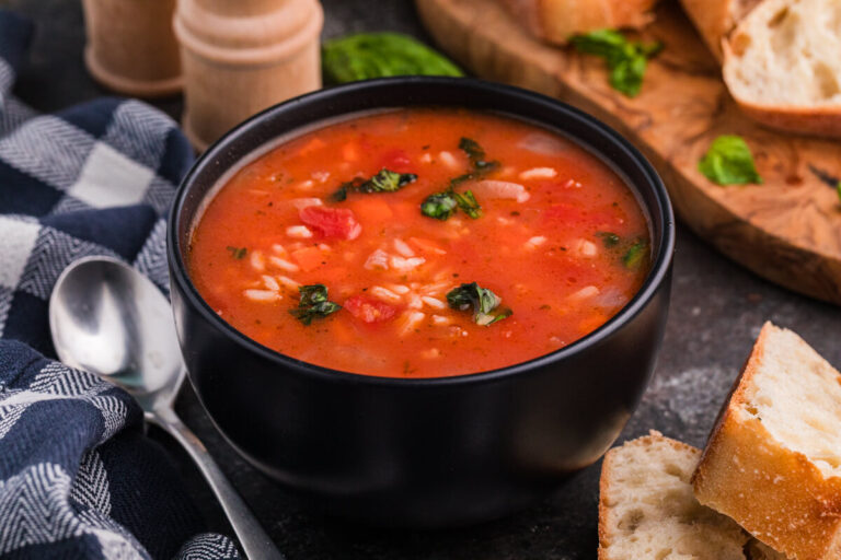 Bowl of vegetable rice soup with tomatoes and herbs, served with crusty bread.