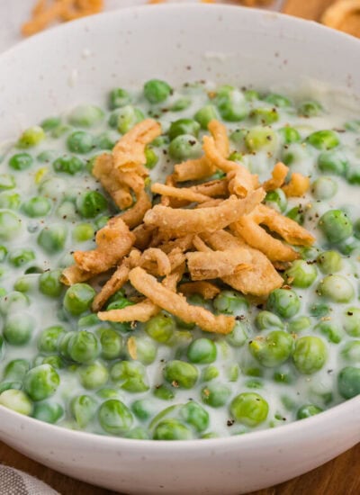 Close-up of creamy green peas in white sauce topped with crispy fried onions in a bowl.