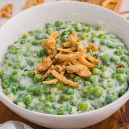 Close-up of creamy green peas in white sauce topped with crispy fried onions in a bowl.