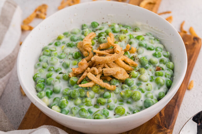 Close-up of creamy green peas in white sauce topped with crispy fried onions in a bowl.