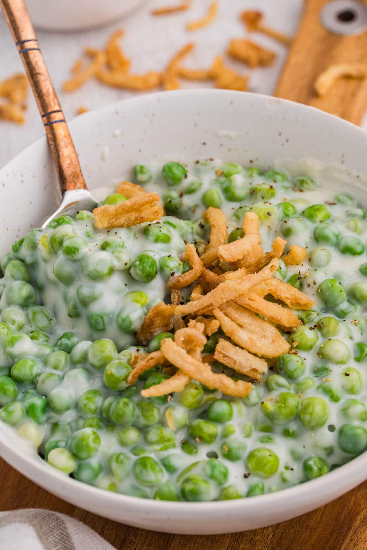 Spoon scooping creamed peas with crispy fried onions from a white bowl.