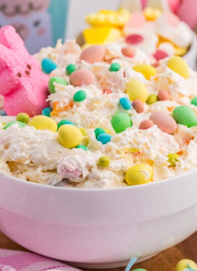 Easter dessert bowl with creamy fluff, pastel candies, marshmallow bunny, and dyed eggs background.