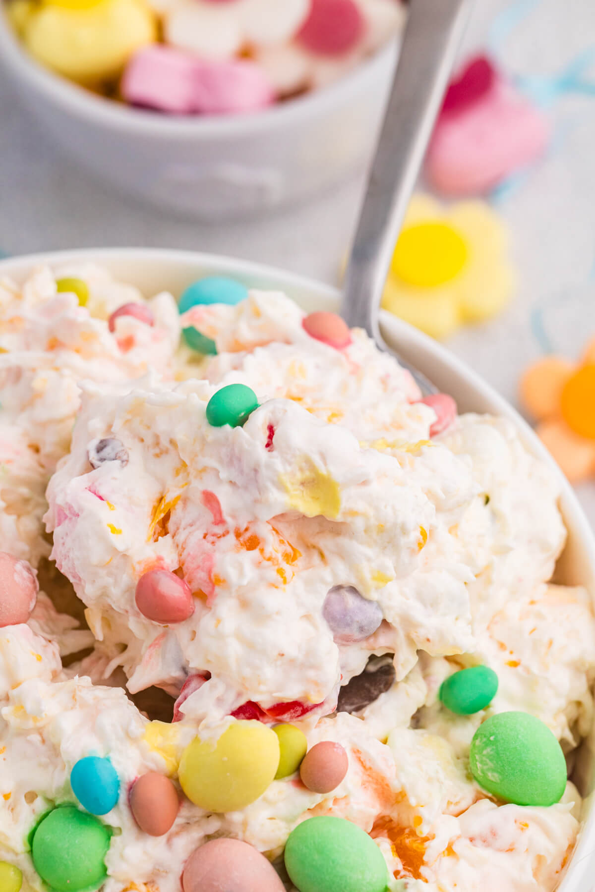 Spoonful of creamy fluff salad with pastel candy-coated chocolates and marshmallows.