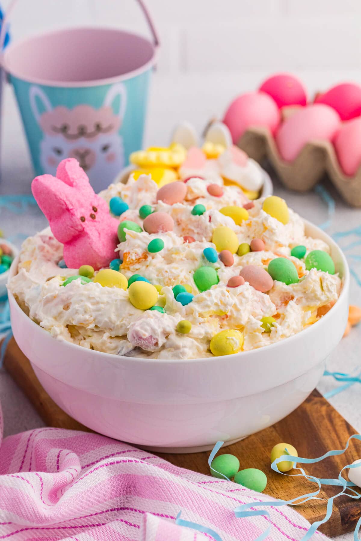 Easter dessert bowl with creamy fluff, pastel candies, marshmallow bunny, and dyed eggs background.