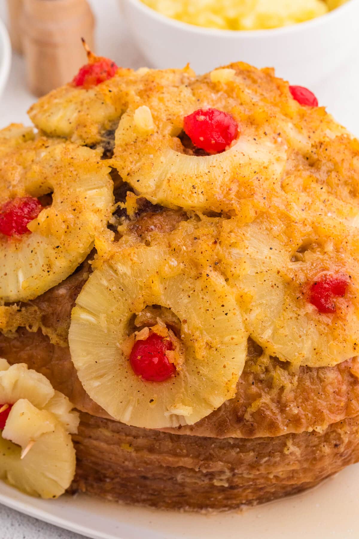 Close-up of roasted ham topped with pineapple slices and maraschino cherries, showcasing juicy texture and sweet glaze.