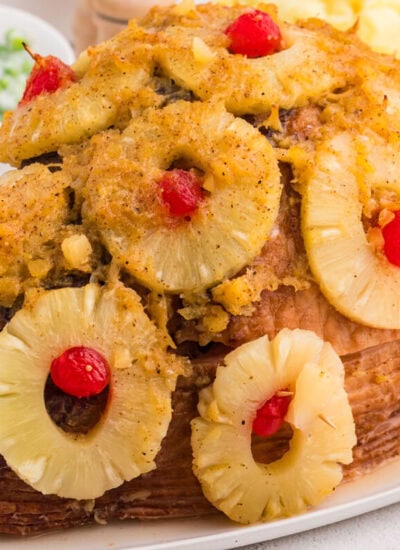 Whole baked ham with pineapple and cherry garnish on white platter, festive holiday meal with classic sweet-savory presentation.