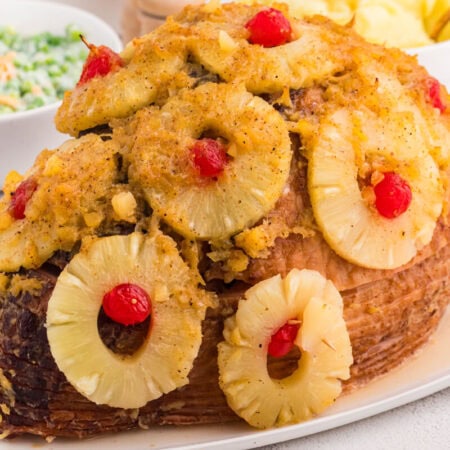 Whole baked ham with pineapple and cherry garnish on white platter, festive holiday meal with classic sweet-savory presentation.