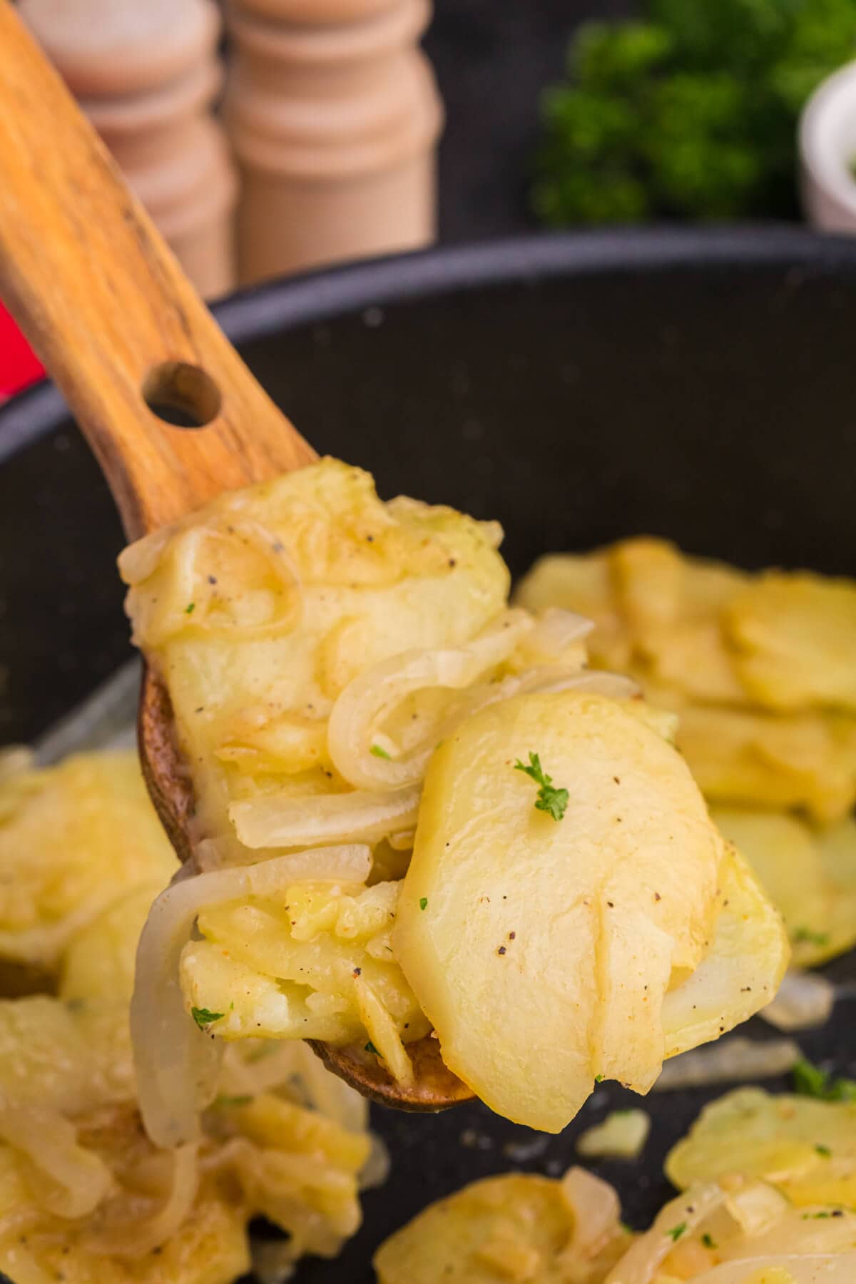 Wooden spoon lifting fried potatoes and onions, showing soft texture and seasoning.