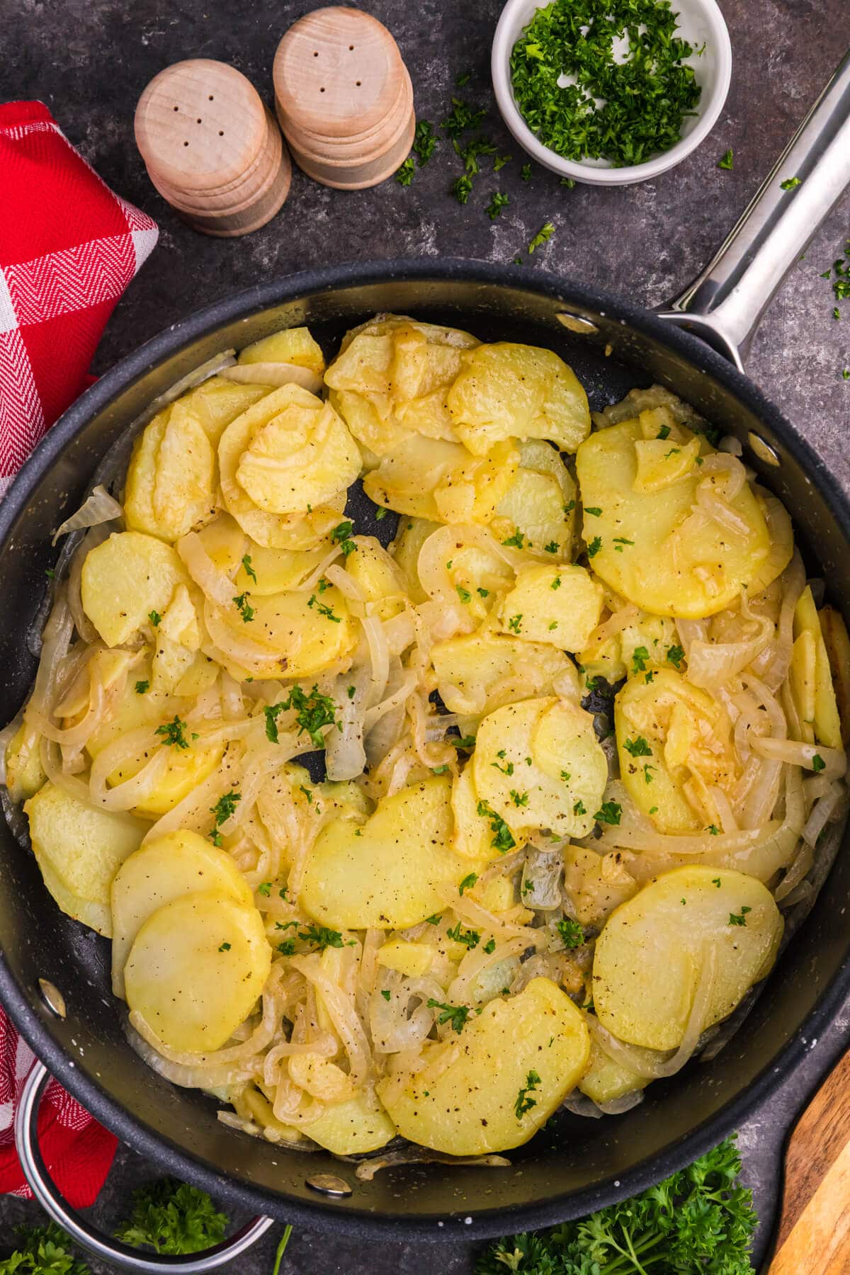 Overhead skillet of fried potatoes and caramelized onions with parsley, rustic setup with spices and red towel.