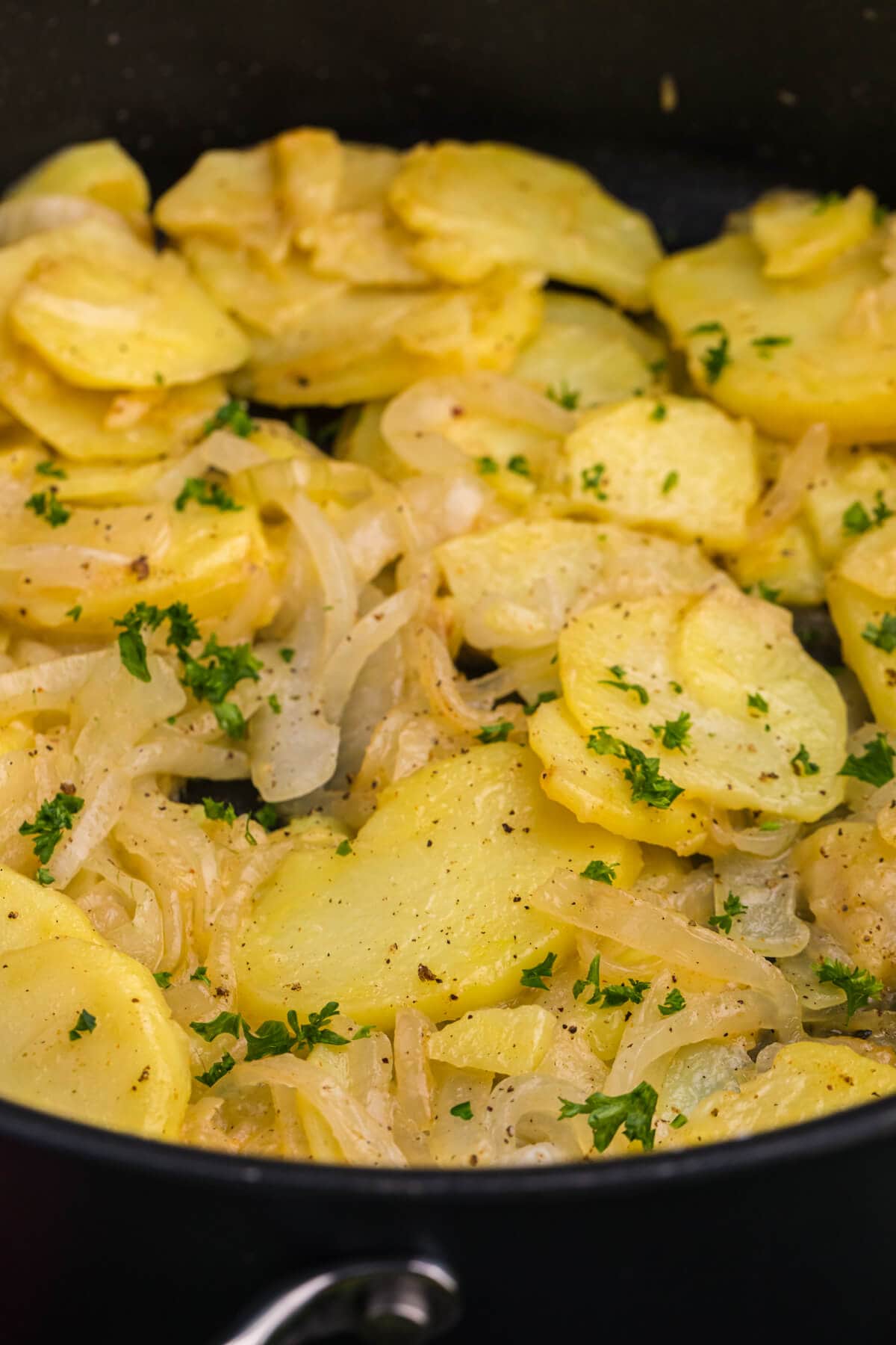Close-up of golden potato slices and caramelized onions with parsley and black pepper.