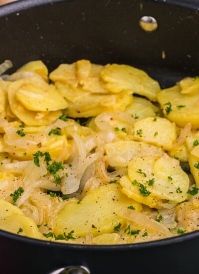 Angled view of saut&eacute;ed potatoes and onions in a black pan with parsley garnish.
