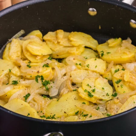 Angled view of sautéed potatoes and onions in a black pan with parsley garnish.