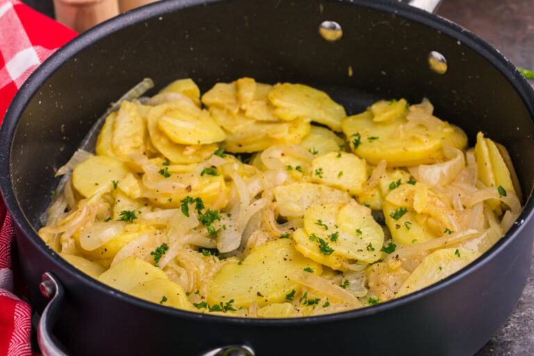 Angled view of sautéed potatoes and onions in a black pan with parsley garnish.