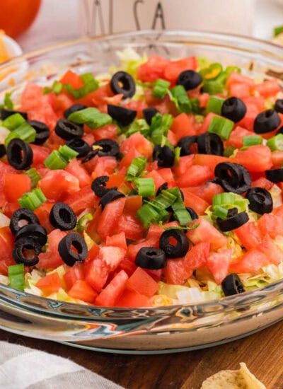 Macro shot of tortilla chip dipped in taco dip with visible layers of sour cream, salsa, shredded cheese, lettuce, and green onions, highlighting creamy texture and fresh toppings.