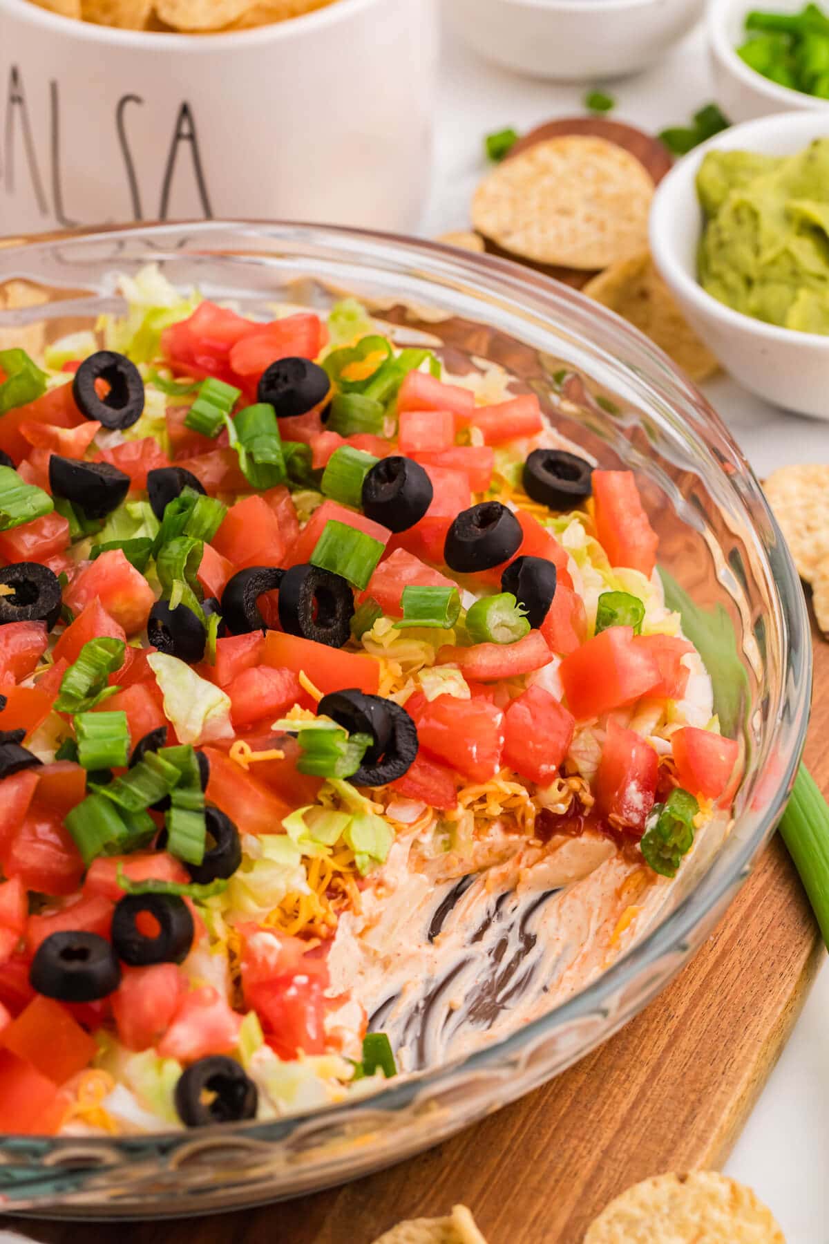 Detailed view of taco dip layers showing creamy base, salsa, cheese, lettuce, and fresh toppings including tomatoes, black olives, and green onions in serving dish.