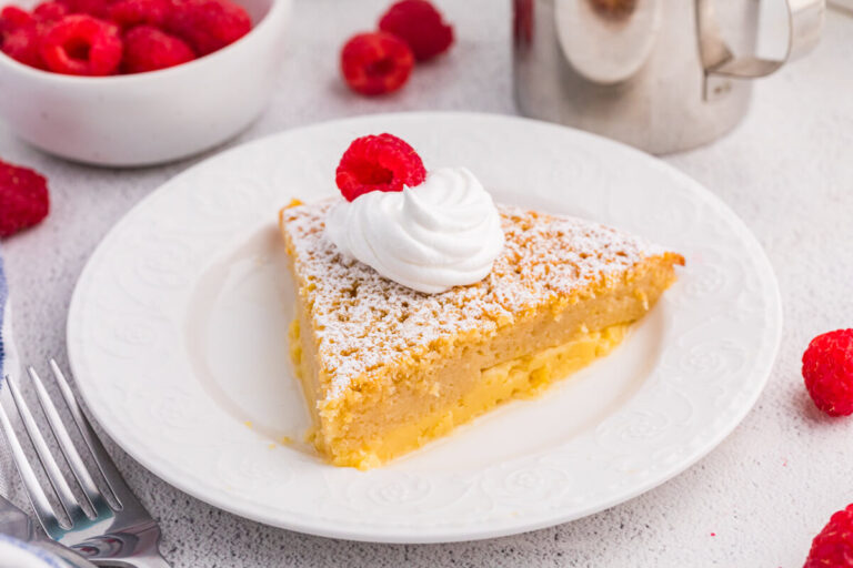 Single slice of impossible buttermilk pie garnished with whipped cream and raspberry, served on a white plate with fresh raspberries nearby.