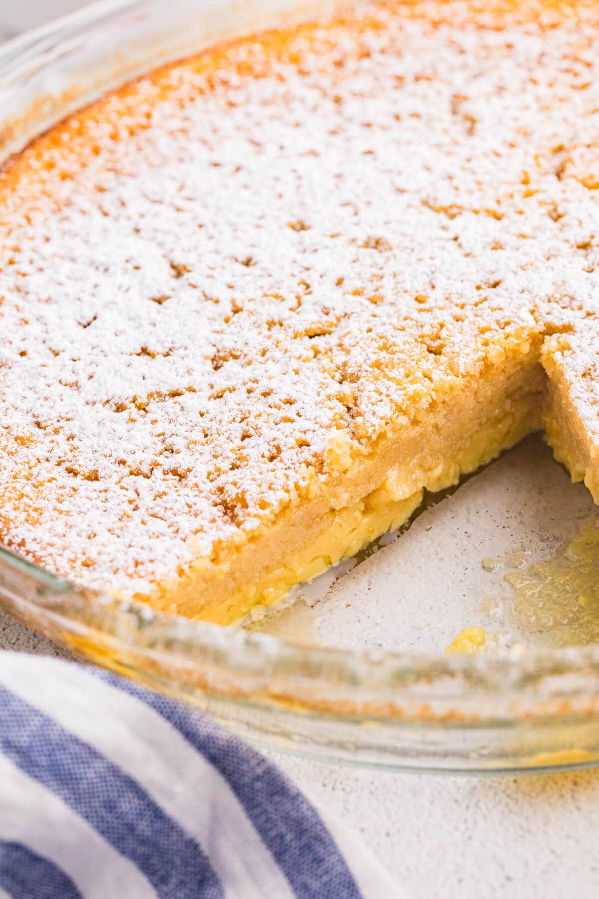 Impossible buttermilk pie with a slice removed, showing the creamy custard filling beneath the golden top dusted with powdered sugar.