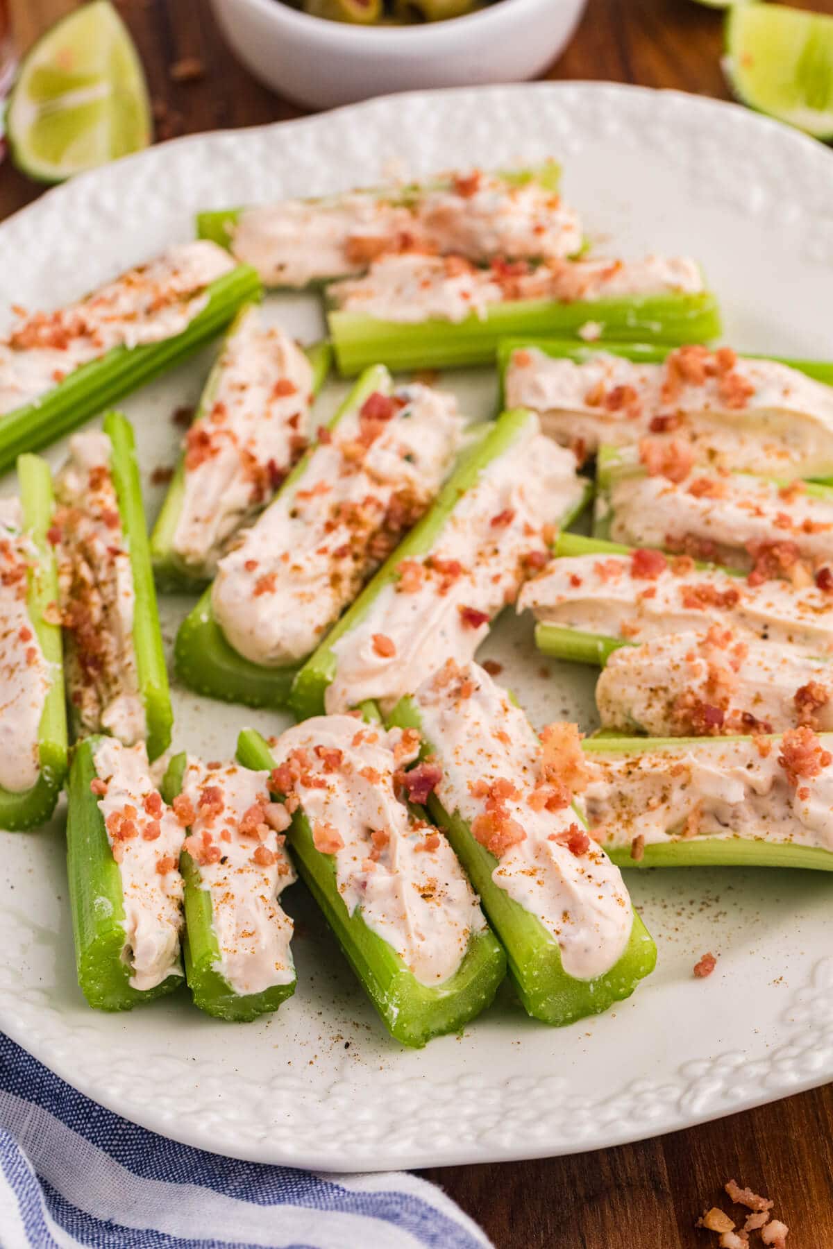 Caesar stuffed celery sticks with creamy filling, bacon crumbles, and seasoning on a white plate with lime wedges.