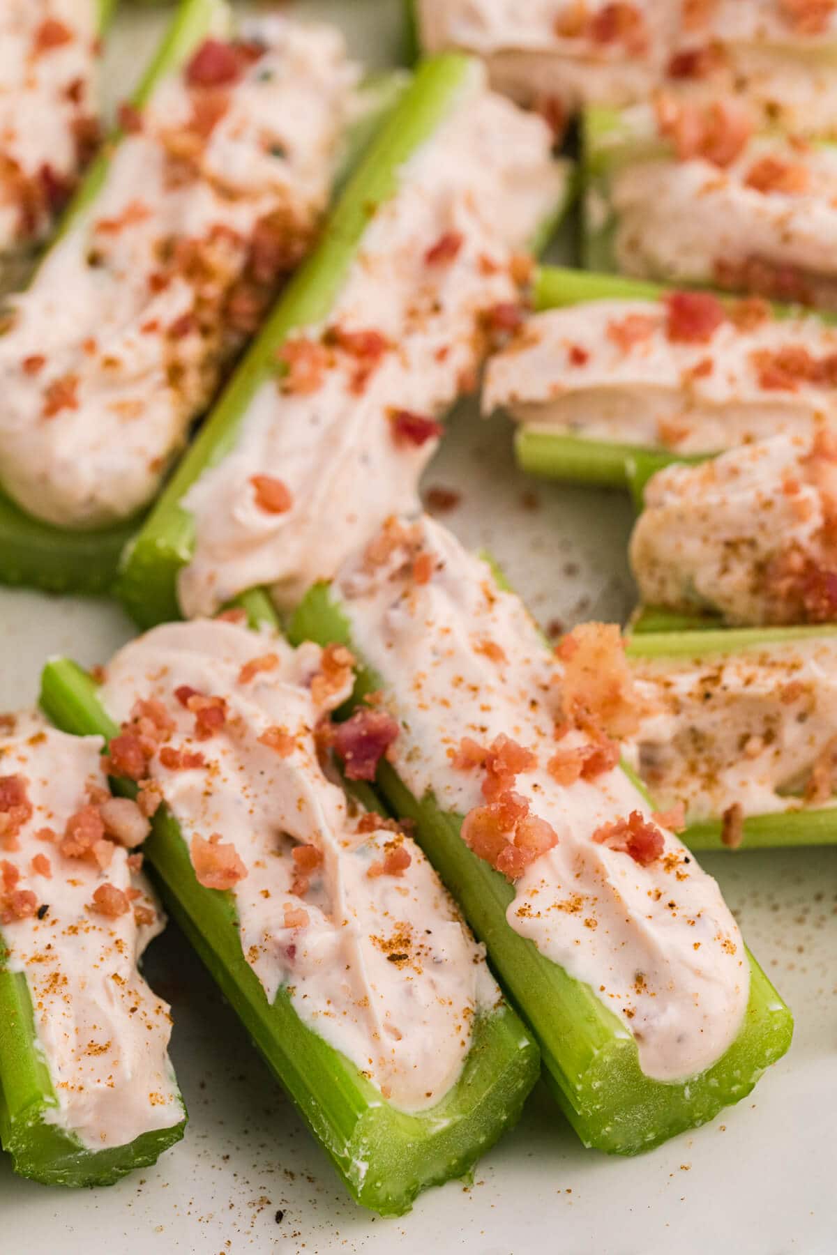 Close-up of Caesar stuffed celery with creamy cheese filling, bacon crumbles, and spices on a white serving plate.