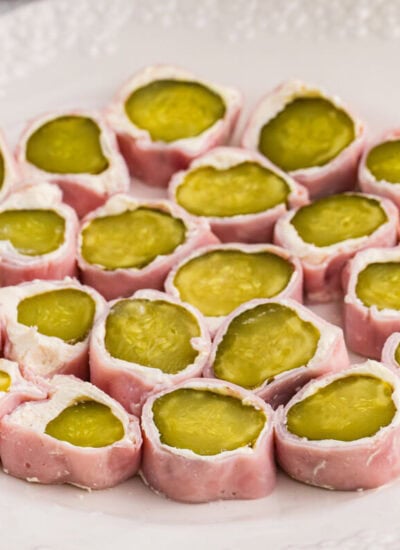 Plate of ham and pickle roll ups sliced into bite-sized appetizers, featuring dill pickles wrapped in cream cheese and deli ham on a white serving plate.