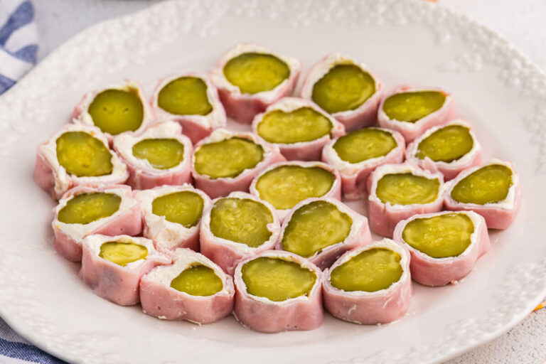 Plate of ham and pickle roll ups sliced into bite-sized appetizers, featuring dill pickles wrapped in cream cheese and deli ham on a white serving plate.