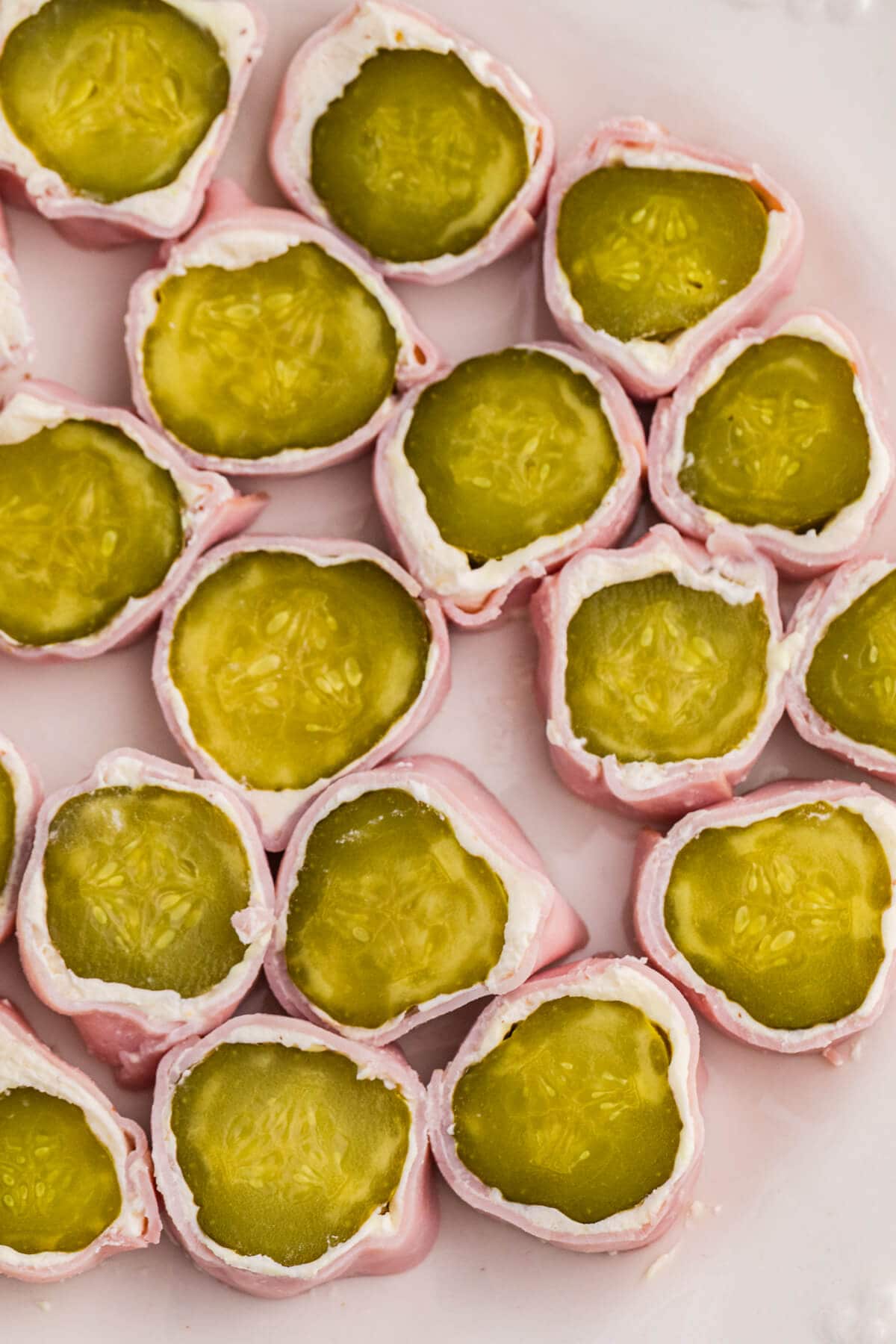 Close-up view of ham and pickle roll ups with creamy cheese filling and dill pickle centers, arranged tightly on a white plate.