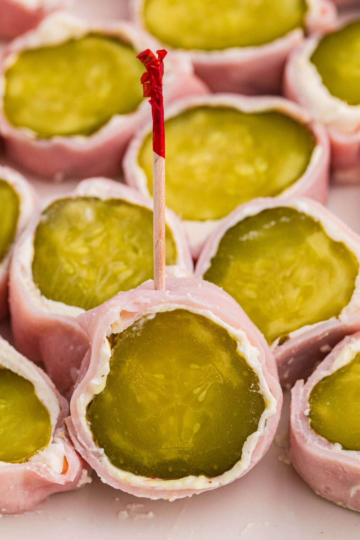Macro photo of a ham and pickle roll up secured with a decorative toothpick, showing layers of deli ham, cream cheese, and dill pickle.