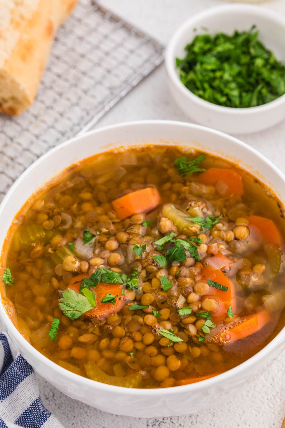 Bowl of lentil soup topped with chopped parsley, with bread and a small bowl of greens in the background.