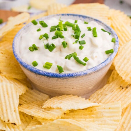 Close-up golden ridged chips surrounding creamy onion dip with fresh chives.