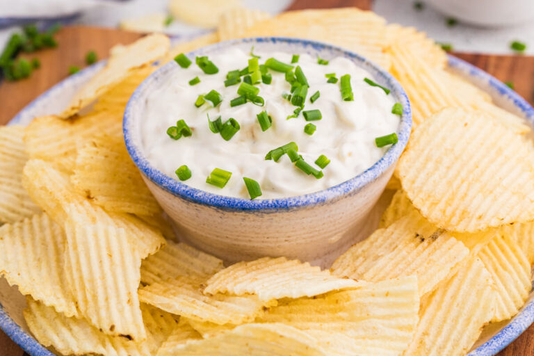 Close-up golden ridged chips surrounding creamy onion dip with fresh chives.