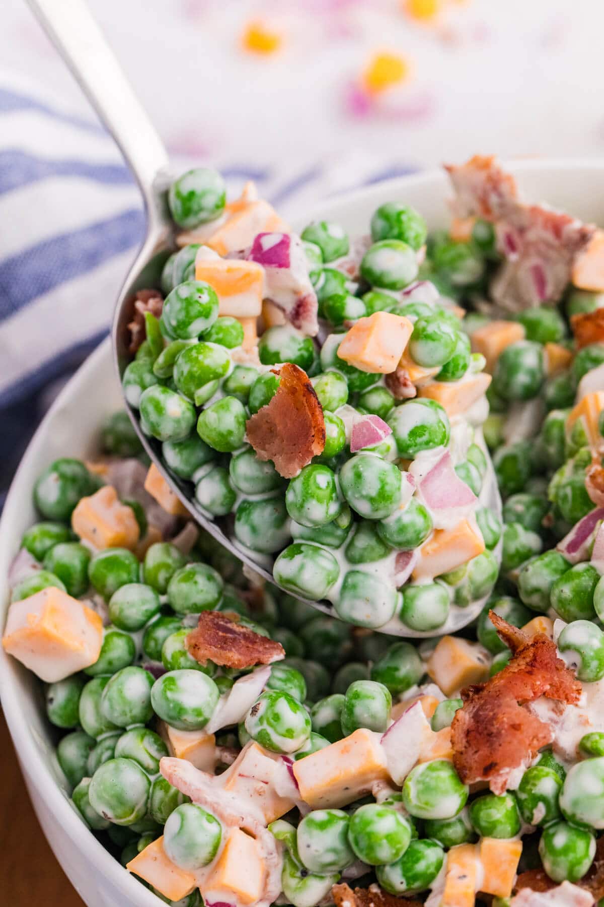 Macro close-up of spoonful of creamy pea salad with green peas, cheddar cheese, crispy bacon, and red onion coated in dressing, detailed texture food photography.