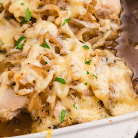 French onion chicken bake topped with melted cheese, caramelized onions, parsley, and herbs in a rich brown pan sauce inside a white casserole dish.