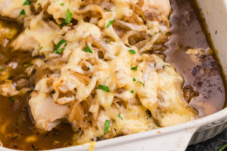 French onion chicken bake topped with melted cheese, caramelized onions, parsley, and herbs in a rich brown pan sauce inside a white casserole dish.