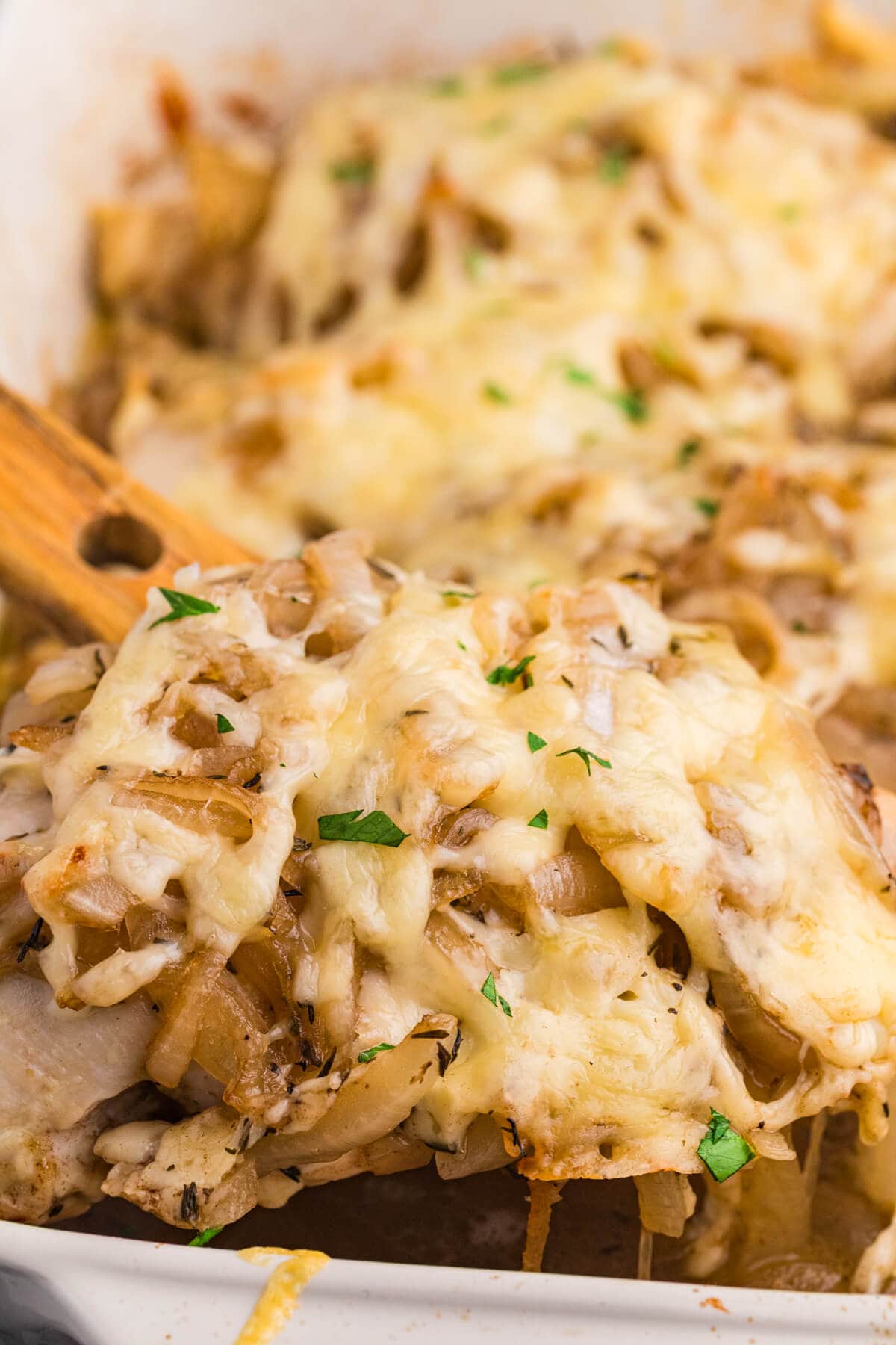 Spoon lifting cheesy French onion chicken bake with caramelized onions and herbs from a casserole dish, showing gooey melted cheese and tender chicken.