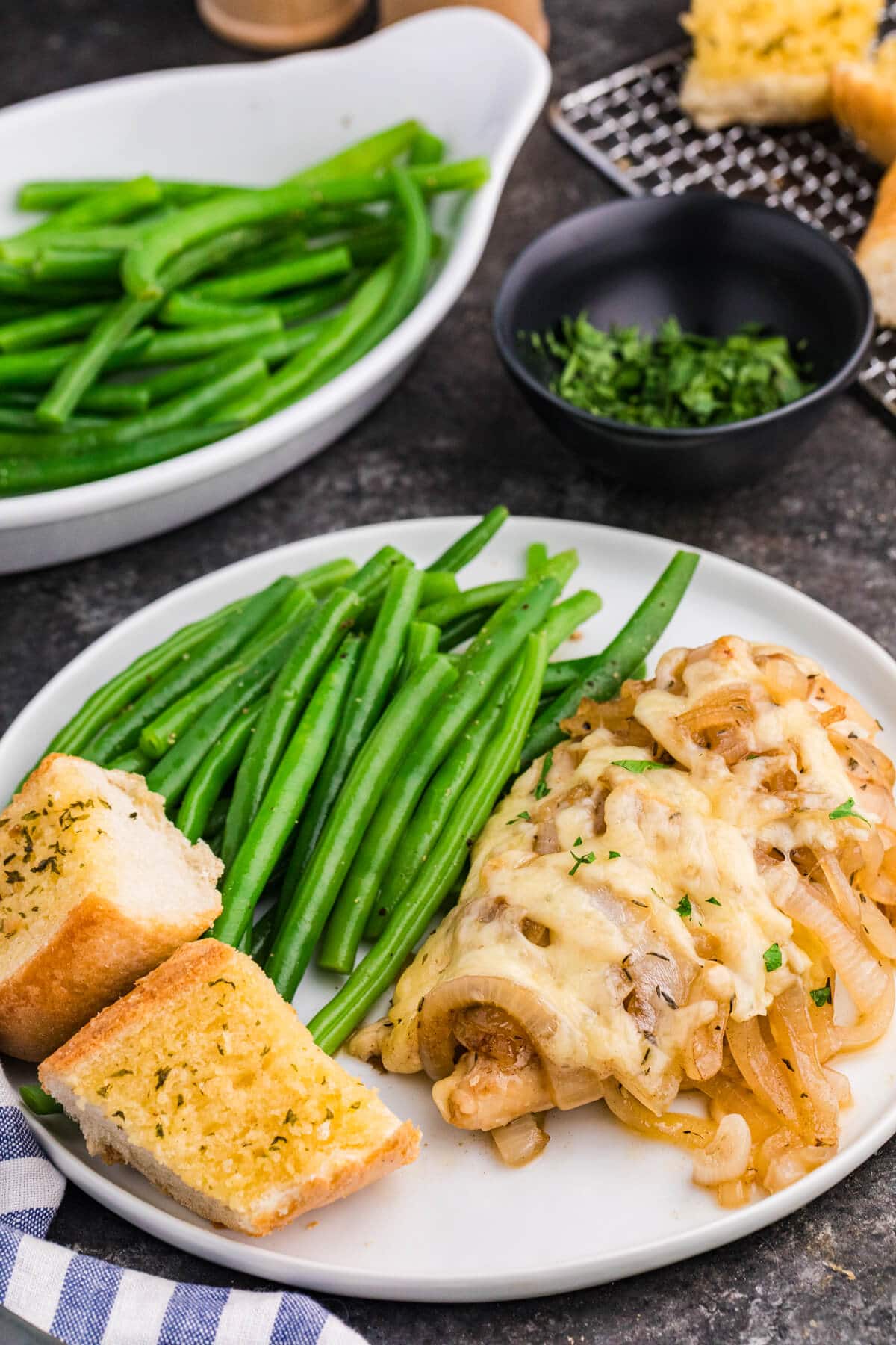 Plated French onion chicken bake with caramelized onions and melted cheese, served with bright green beans and garlic bread on a white dinner plate.