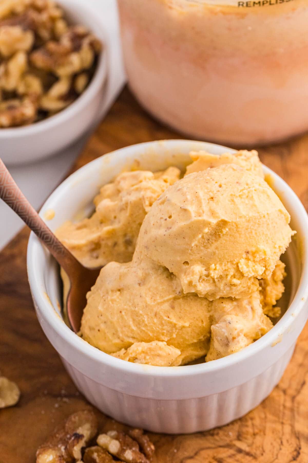 Carrot cake ice cream scooped into a white bowl with walnuts and the Ninja Creami pint in the background.