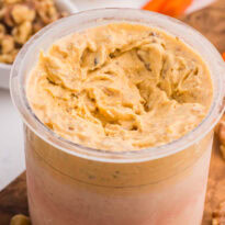 Carrot cake ice cream in a Ninja Creami pint with walnuts and carrot sticks on a wooden board.