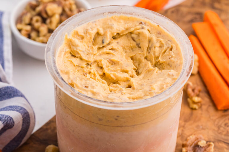 Carrot cake ice cream in a Ninja Creami pint with walnuts and carrot sticks on a wooden board.