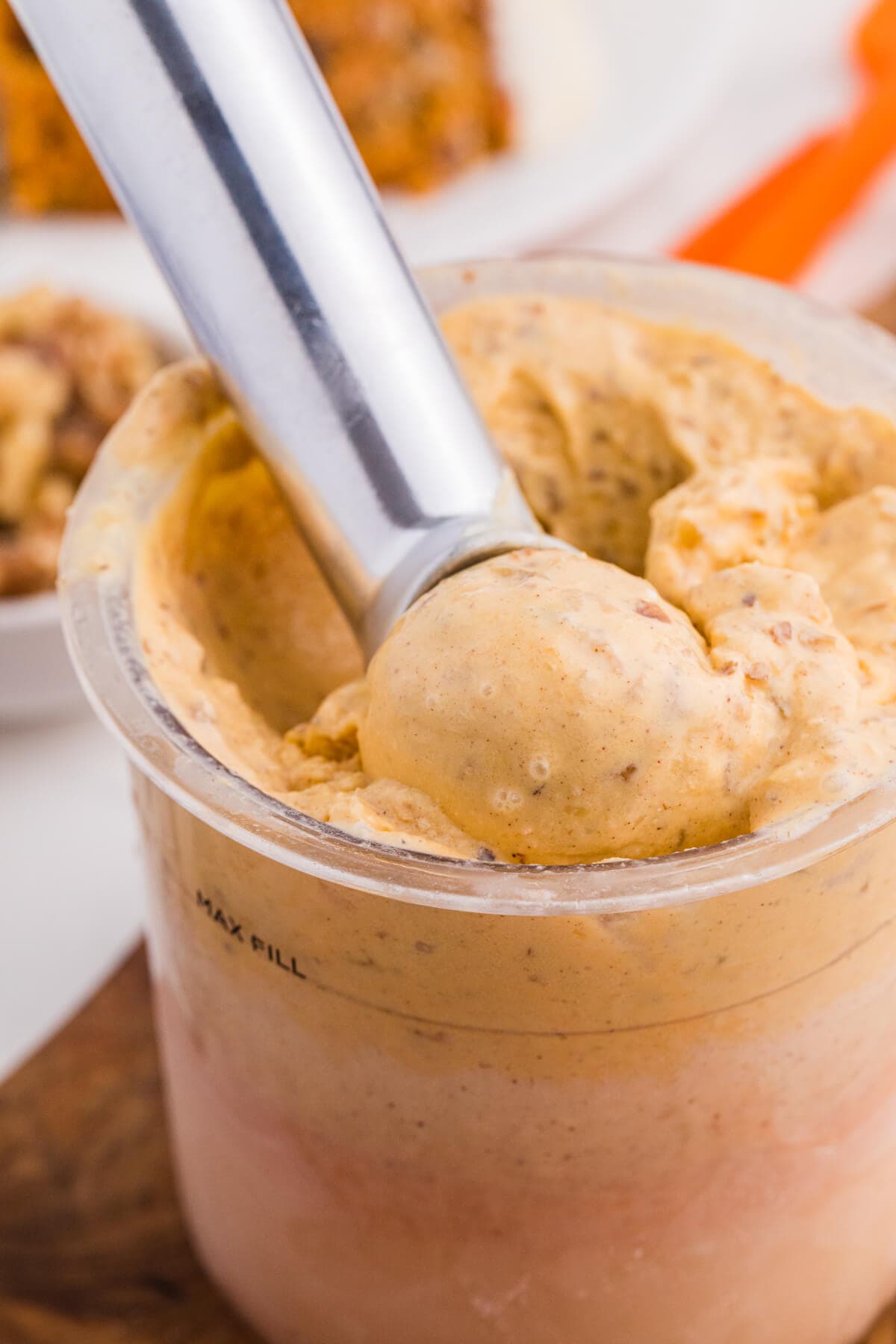 Carrot cake ice cream being scooped from a Ninja Creami pint with carrot cake and walnuts in the background.